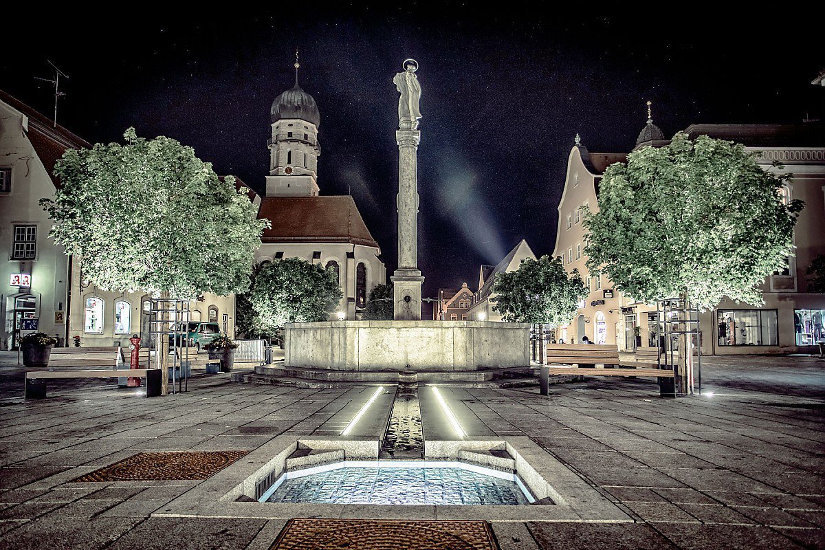 Schongau in Oberbayern - Immobilien kaufen und verkaufen im Herzen der historischen Altstadt Marktplatz Schongau bei Nacht - Mariensäule und Brunnen mit Blick auf die Stadtpfarrkirche St. Maria Himmelfahrt, beleuchtet unter Sternenhimmel